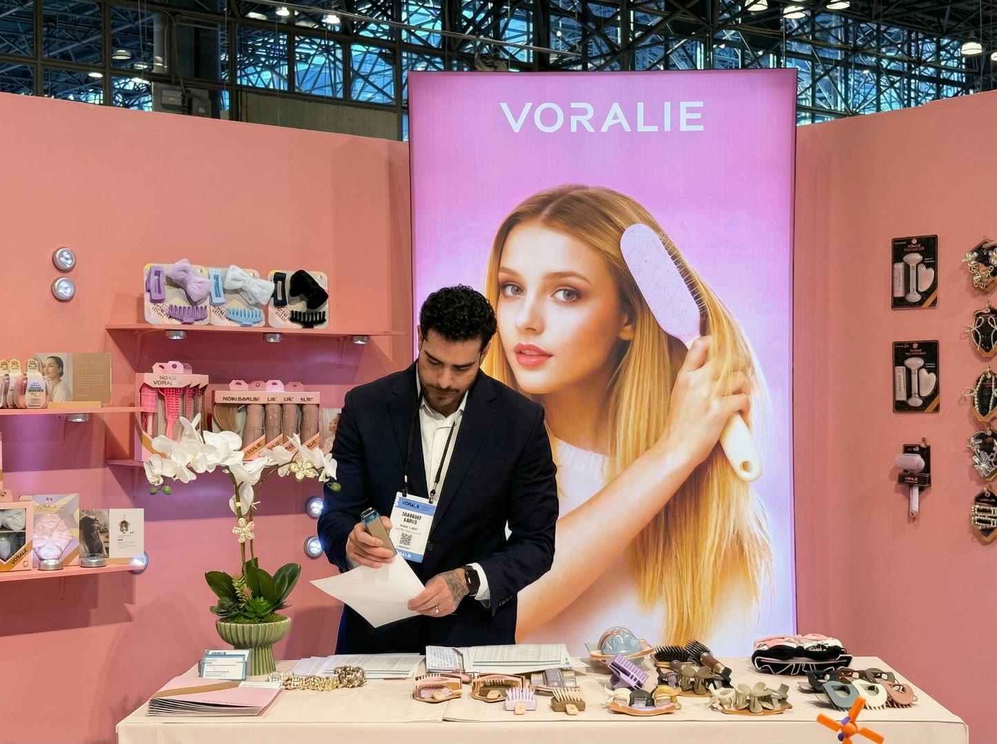 Voralie booth at NY NOW — salesperson at pink Voralie wall with products and buyer materials